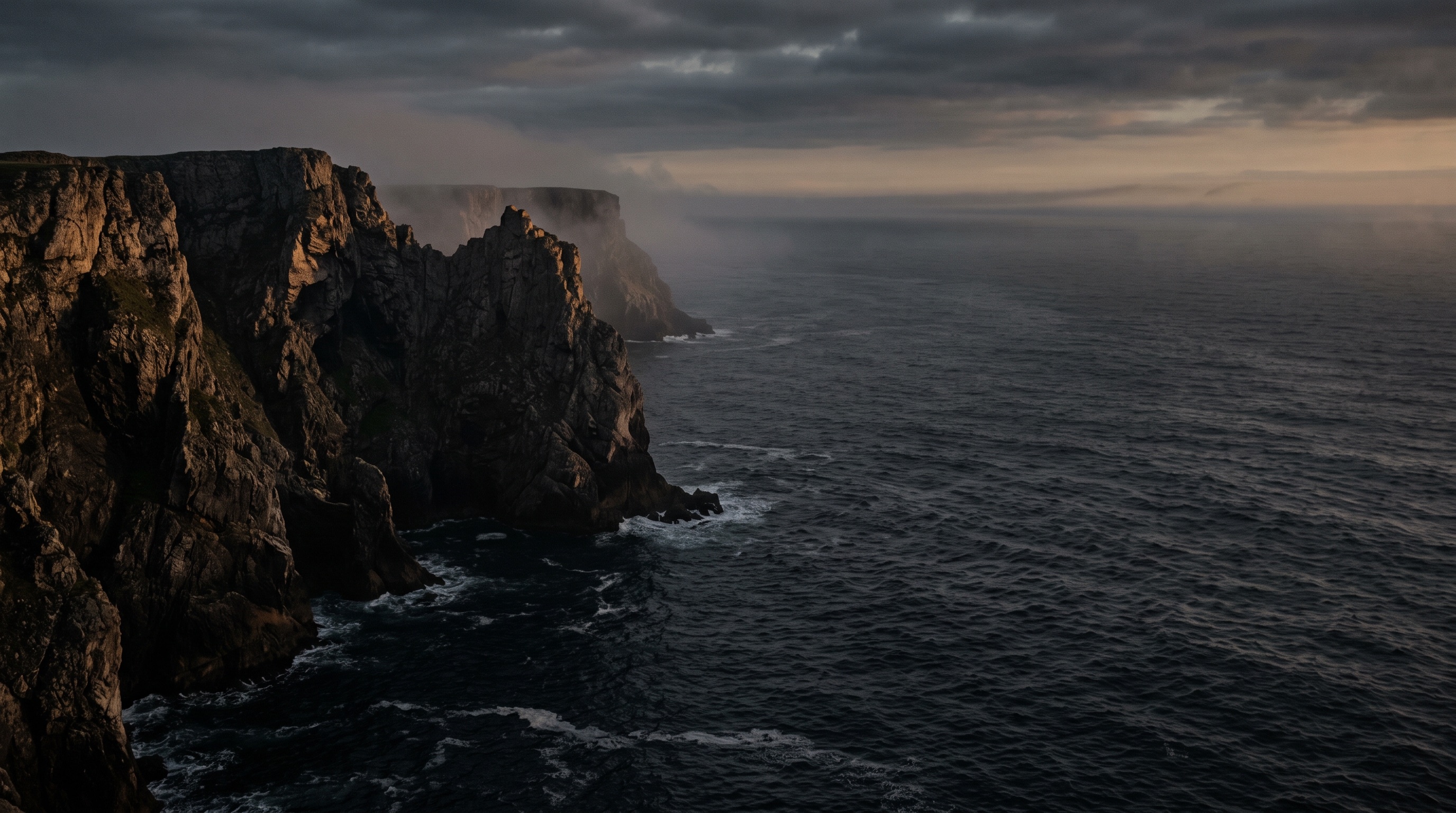 Dark limestone cliffs falling into a slate sea, in thin mist.